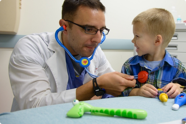 doctor using toy stethoscope pretending to check little boy's heart