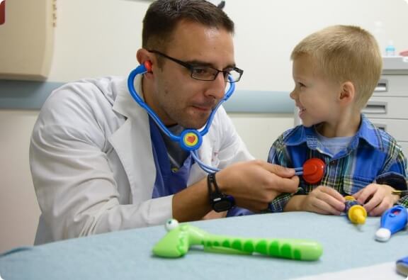 pediatrician using toy stethescope to check boy patient's heart